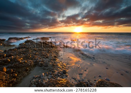 Early morning landscape of ocean over rocky shore with glowing sunrise