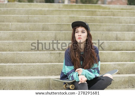 Portrait of hipster young woman with skateboard sitting on stairs in the street.