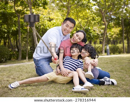 happy asian family with two children taking a outdoor selfie with selfie stick outdoors in a city park.