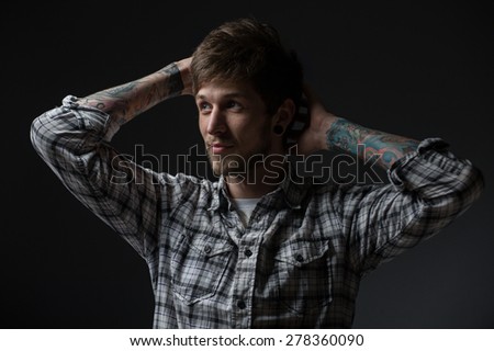 young man looks to the right, and ponders. On his hands he's got tattoos , and piercings in the ears