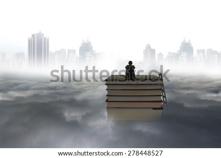 Pondering business man sitting on stack of books with city landscape gray cloudscape background