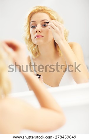 A picture of a young woman applying eye shadow in the bathroom