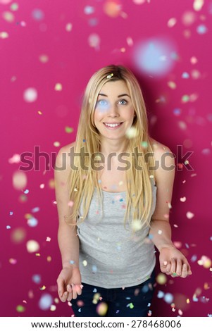 Pretty Young Blond Woman Looking Up to Falling Confetti While Standing Against Pink Background.
