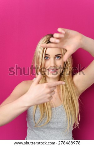 Close up Smiling Blond Girl in Casual Outfit Framing her Pretty Face with Hands, Isolated on Dark Pink Background.
