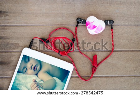 Portable audio earphones with asian baby screen in tablets and heart soap on wood background