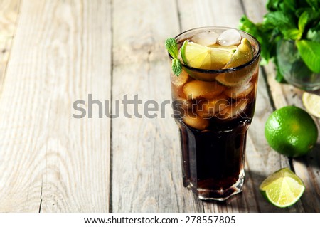 Cocktail with cola, mint, lime and ice on wooden table
