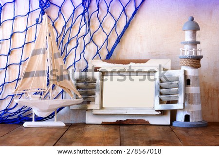 old vintage wooden white frame, lighthouse and sailing boat on wooden table. vintage filtered image. nautical lifestyle concept
