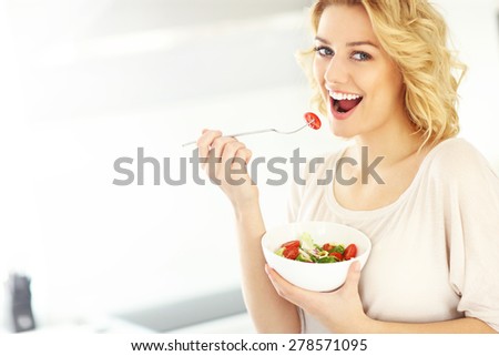 A picture of a young woman eating salad in the kitchen