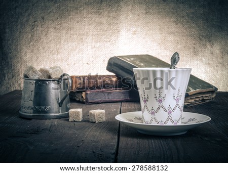 Cup of coffee, sugar bowl and stack of old books on the old wooden table.