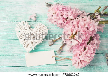 White decorative heart with hyacinths, willow flowers and empty tag  on turquoise painted wooden background. Empty place  for your text. Toned image.