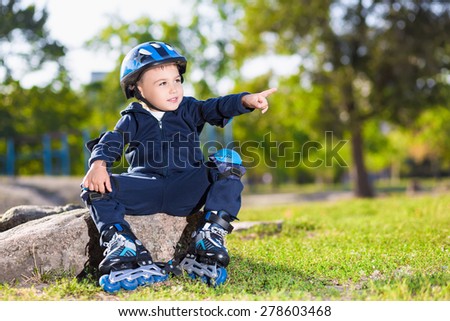 Little skater boy sitting on the stone in a park and pointing towards