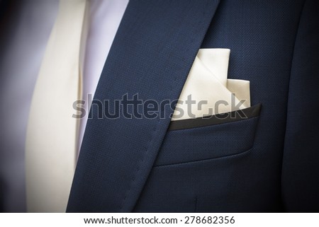 Elegant blue stylish jacket with handkerchief peeking out of the pocket and with white tie; a wedding suit. Vignetting enhanced in post production.