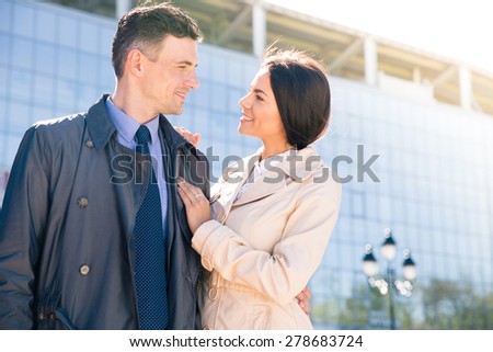 Happy couple standing outdoors and looking to each other with glass building on background