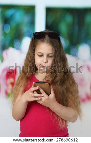 Little girl with long hair looks skeptically to smartphone in her hands - communication and modern technology concept