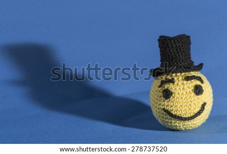 Knitted yellow emoticon with bowler on blue background