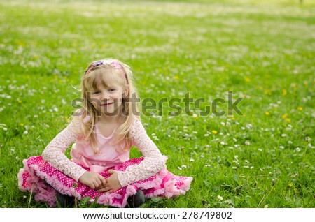 adorable blond girl sitting in green meadow with white daisies