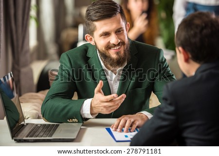 Two confident businessmen in suits working on project and using laptop in cafe.