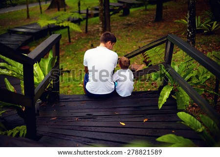 father and son sitting on wooden stairs in rain forest