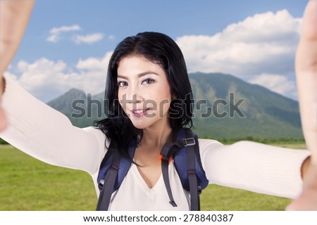 Beautiful young woman takes selfie picture on the mountain while carrying backpack