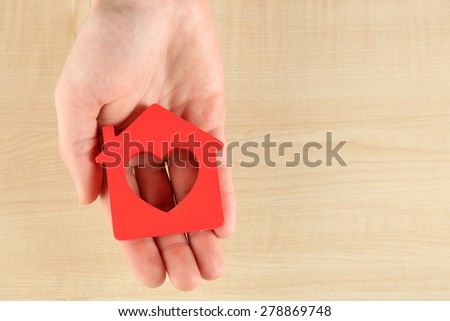 Female hand holding house on wooden background