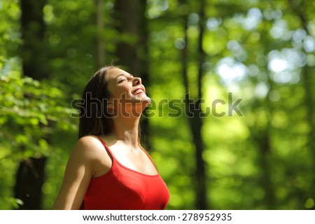 Woman breathing fresh air in a green forest in summer wearing a red shirt