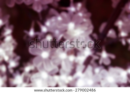 blurry defocused image of white light in flower shape decorating on fake tree with bokeh for background