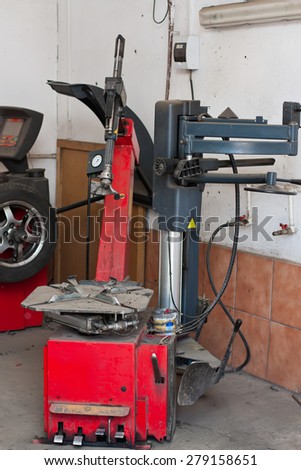 A tire changer device in an automobile repair shop, with a wheel balancing machine in the background.