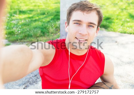 Sitting guy in a basketball court and take a selfie after match with friends - listen music with headphones - Blond man finish to do sport and make himself picture 