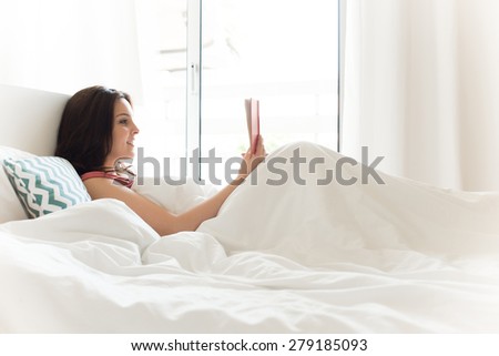 Woman reading book in bed during the morning
