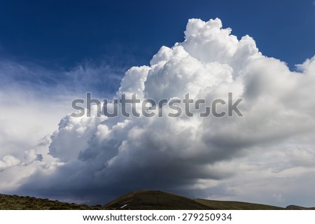 Storm cloud over the mountain ridge against the blue sky.
