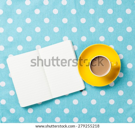 Cup of coffee and notebook on blue polka dot background.
