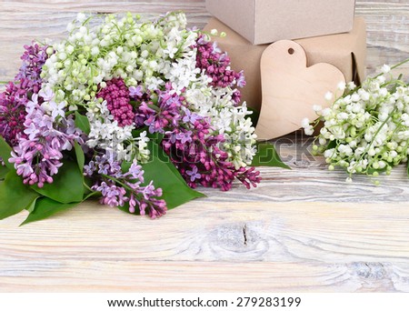 Charming spring flowers of a lilac and lilies of the valley and gift boxes on a wooden background. A background for the subject "holiday" with space for the text.