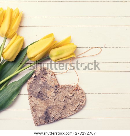 Fresh aromatic  yellow tulips flowers  and rustic decorative heart on white painted wooden background. Selective focus. Place for text. Toned image.