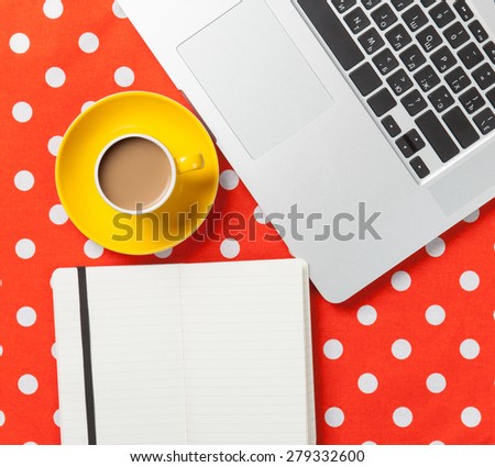 Cup of coffee and notebook near laptop computer on red polka dot background