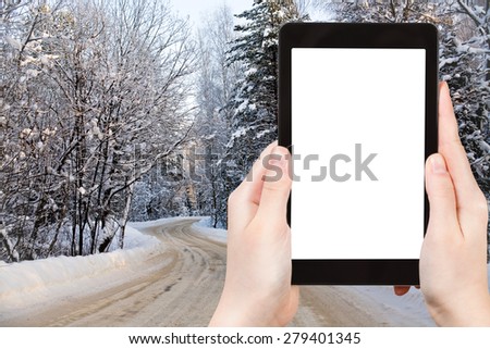 travel concept - tourist photograph country road in snowy russian forest on tablet pc with cut out screen with blank place for advertising logo