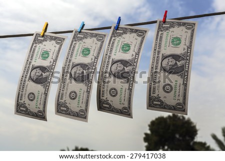 Four american dollars drying on string with sky and trees in the background
