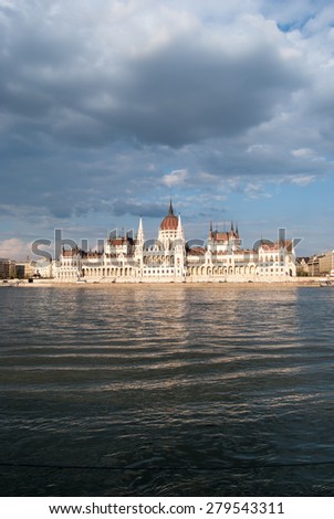 Gorgeous view of Budapest Parliament building in sunset under big clouds, near glittering water of Danube. Travel background picture of Hungary.