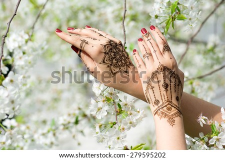 Red manicured hands with Mehndi in spring cherry blossom, Indian tradition. Horizontal composition.
