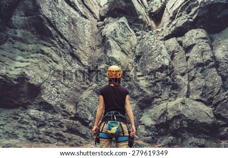 Young woman wearing in climbing equipment standing in front of a stone rock outdoor and preparing to climb, rear view Royalty-Free Stock Photo #279619349