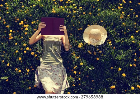 Girl lying in grass, reading a book. Intentionally toned. Royalty-Free Stock Photo #279658988