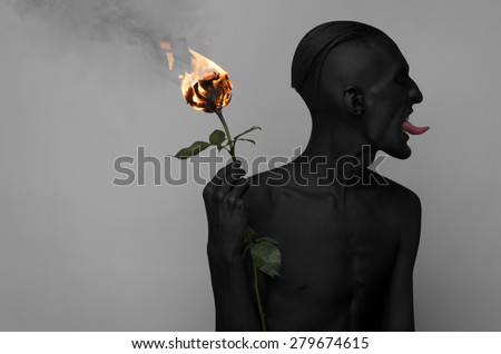 Gothic and Halloween theme: a man with black skin holding a burning rose, black death isolated on a gray background in studio