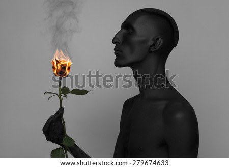 Gothic and Halloween theme: a man with black skin holding a burning rose, black death isolated on a gray background in studio