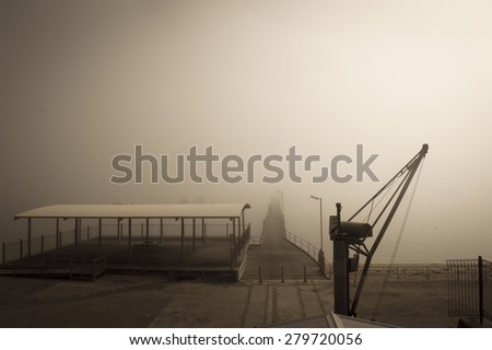 Filtered image of foggy harbour at ocean or lake or river water with crane and wooden jetty, blurred background and copy space. Royalty-Free Stock Photo #279720056