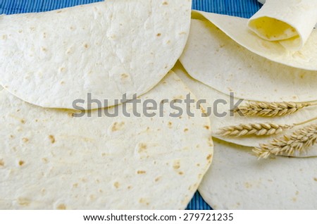 Fresh tortillas and a stick of wheat on a blue tablecloth