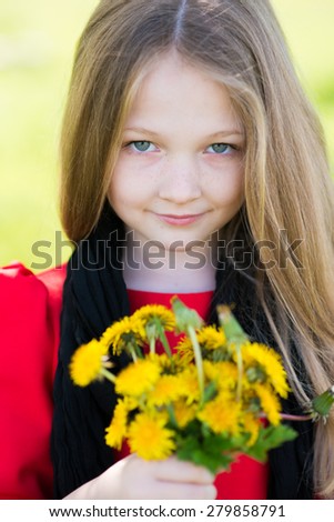 The little girl in a red dress standing outdoors in the garden and holding flowers