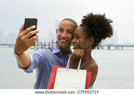 Black tourist heterosexual couple in Casco Antiguo Panama City with shopping bags. The man takes a selfie with his girlfiend and shopping bags with skyline in background