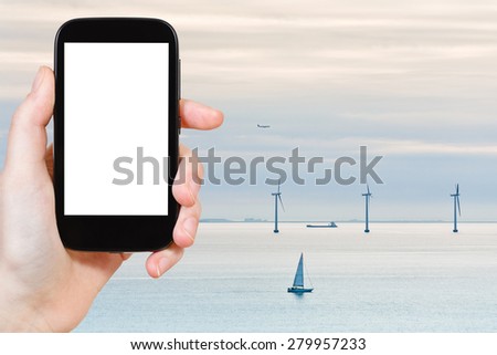 travel concept - tourist photograph Middelgrunden offshore wind farm near Copenhagen, Denmark at early morning on smartphone with cut out screen with blank place for advertising logo
