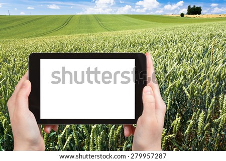 travel concept - tourist photograph green wheat field in Normandy, France on tablet pc with cut out screen with blank place for advertising logo