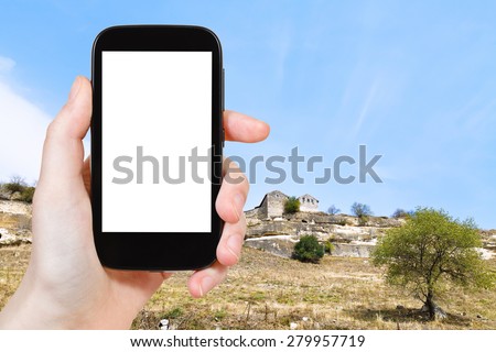 travel concept - tourist photograph medieval town chufut-kale on mountains of gorge mariam-dere in Crimea on smartphone with cut out screen with blank place for advertising logo