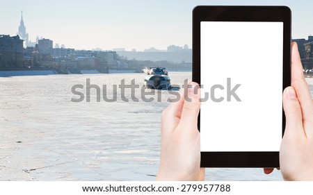 travel concept - tourist photograph iceboat on frozen Moscow river in sunny winter day on tablet pc with cut out screen with blank place for advertising logo